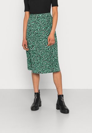Jupe midi à motifs verts en tissu léger, dotée d'une taille élastique et d'une coupe droite, associée à des bottines noires.