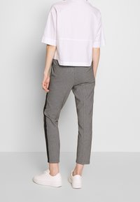 Ljust rosa kortärmad skjorta, kombinerad med svartvita rutiga byxor med en solid svart sidostrand, bärs med vita sneakers.