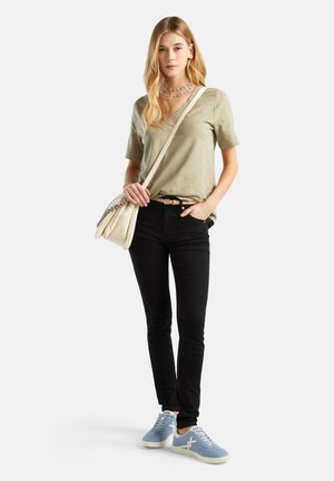 Olivově zelené tričko s výstřihem do V, černé skinny džíny, světle modré tenisky. Modelka nese krémovou kabelku přes rameno s řetízkovými detaily.