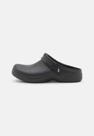 Zuecos de goma negros con punta redondeada, correa trasera ajustable, suela texturizada y acabado suave, diseñados para la comodidad y fácil uso.