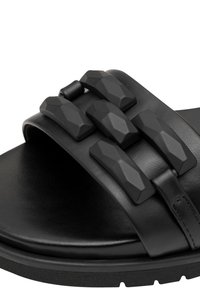 Schwarze Riemensandale mit glänzender Lederoberfläche, drei strukturierten Gummiriemen mit geometrischem Design und gepolsterter Innensohle.
