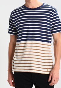 Pruhované tričko s krátkým rukávem v námořnické, bílé a hnědé barvě; kulatý výstřih; hladká bavlněná tkanina; malá logo aplikace.