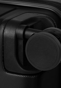 Valigia rigida nera con superficie testurizzata, dotata di un robusto sistema di ruote nere e di un design circolare delle ruote.