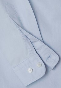 Světle modrý košilový rukáv s dvěma bílými knoflíky, diagonálním švem a hladkým textilem.