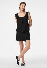 Abito nero con scollatura quadrata, spalline arricciate e design a strati. Tessuto morbido con una gonna aderente e scarpe nere basse.