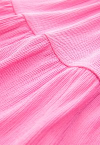 Różowa teksturowana tkanina z pionowymi paskami, z miękkimi plisami. Powierzchnia wydaje się lekko pognieciona, co podkreśla jej dotykową jakość.