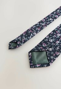 Granatowy krawat w kwiatowy wzór w odcieniach różu i bieli, wykonany z gładkiego materiału. Ma jednolitą zieloną stronę wewnętrzną oraz spiczaste końcówki.