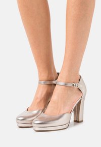 Metalické stříbrné lodičky na vysokém podpatku s zaoblenou špičkou, páskem kolem kotníku s přezkou, platformou a hladkým povrchem.