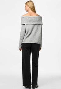 Suéter gris sin hombros con cuello acanalado, fabricado en una suave mezcla de lana, combinado con pantalones de pierna ancha negros, terminado con zapatos planos.
