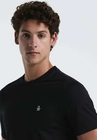 Zwarte t-shirt met korte mouwen en een ronde hals, met een klein wit pinguïnlogo op de linkerborst en een gladde, getailleerde stof.