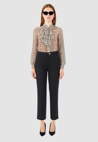 Blusa con stampa leopardata e fiocco, tessuto trasparente; pantaloni neri con righe sottili, design aderente, dettagli con bottoni dorati; abbinati a occhiali da sole neri a forma di gatto.