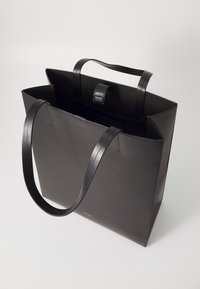 Sac fourre-tout en cuir noir avec deux longues anses, de forme rectangulaire, au design minimaliste, doté d'un rabat à l'avant et d'un intérieur ouvert.