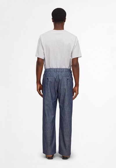 Man standing facing away wearing a light gray short-sleeve shirt and blue elastic-waist wide-leg pants with back pockets.