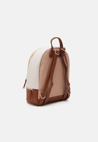 Petit sac à dos bicolore avec panneaux beige et blanc, bretelles d'épaule marron réglables, fermetures éclair dorées et poignée de transport supérieure.