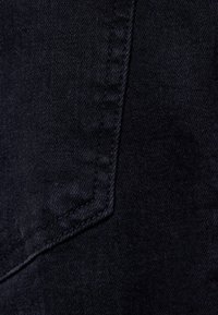 Mörkt denimtyg med en subtil textur, med en diagont söm och kontrasterande sömnad längs kanten. Färgen är en djup marinblå.