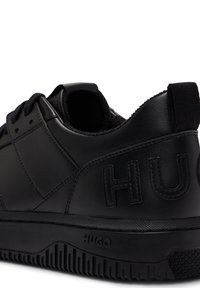 Svarta lädersneakers med en texturerad matt yta, vadderad krage och präglad "HUGO" branding på sidan och hälen.