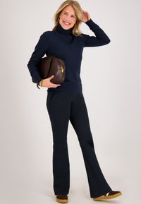 Navy coltrui, slim-fit navy broek en een bruine leren handtas. Model draagt bruine schoenen met lichte zolen. Gladde textuur.