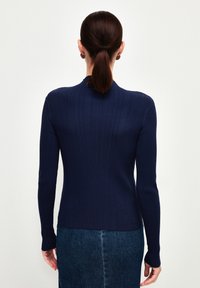 Marinblå ribbstickad tröja med hög nacke och långa ärmar, tillsammans med en denimkjol. Tyget har en slät textur och en åtsittande design.