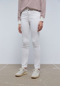 Witte denim skinny jeans met een gladde textuur, gedragen met een langwerpig shirt met rode strepen en lichte sneakers, staand gepresenteerd.