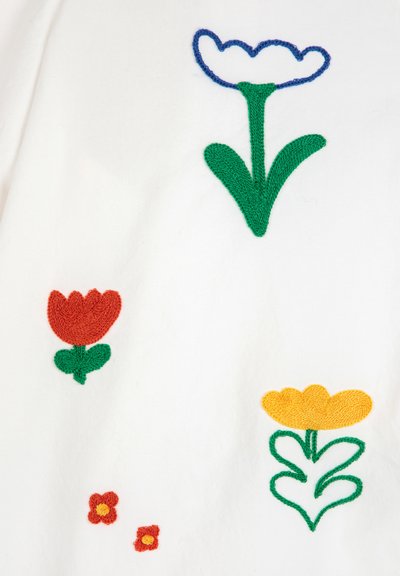 Witte stof met kleurrijke bloemborduurwerk: blauwe, witte en groene tulp; rode en groene bloem; gele bloem met groene accenten; kleine rode en gele bloemen.