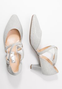 Scarpe con tacchi alti in glitter argento con punta affusolata, dotate di cinturini alla caviglia e tomaia testurizzata. Dettagliate con un accento metallico lucido.