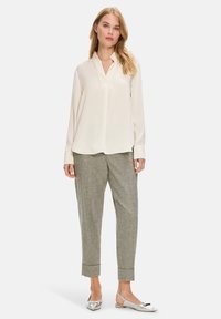 Weiße Seidenbluse mit Reverskragen, kombiniert mit grauen karierten, schmal zulaufenden Hosen und silbernen Slippern. Strukturierter Stoff, lässige Passform.