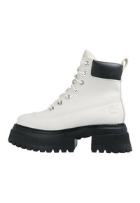 Botine din piele albă până la gleznă, cu accente negre, vârf rotund, sistem de șireturi în față, talpă groasă din cauciuc negru cu striații și logo pe lateral.
