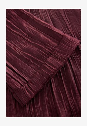 Burgundski plisirani materijal s mekim sjajem, s okomitim teksturama, urednim rubom i suptilnim varijacijama dubine boje.
