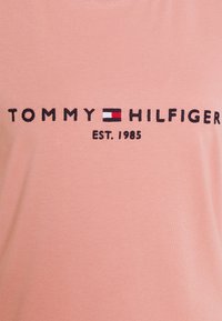 Camiseta de algodón rosa con bordado en negro que dice "TOMMY HILFIGER" y un pequeño logotipo en rojo, blanco y azul encima de "EST. 1985."