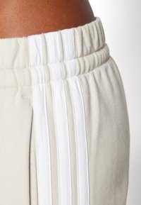 Ljusbeige sweatpants med en texturerad midja och dubbla vita sidostråk. Har ett mjukt tyg och elastiska muddar för komfort.