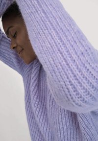 Lila gestrickter Pullover mit geripptem Muster und übergroßen Ärmeln, der ein weiches, flauschiges Aussehen aufweist. Keine auffälligen Muster oder Hardware sichtbar.