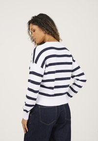 Sweter w paski w odcieniach granatu i bieli o luźnym kroju, z ściągaczem w pasie i mankietach, dzianinowej fakturze, z dekoltem w kształcie litery V i opuszczonymi ramionami.