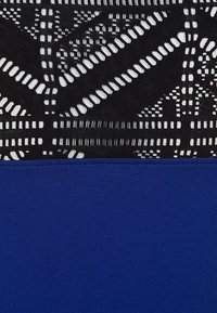 Svart spets tyg med geometriska utskärningar upptill och solid kunglig blått tyg nedanför. Texturerad kontrast mellan den delikata spetsen och det släta tyget.