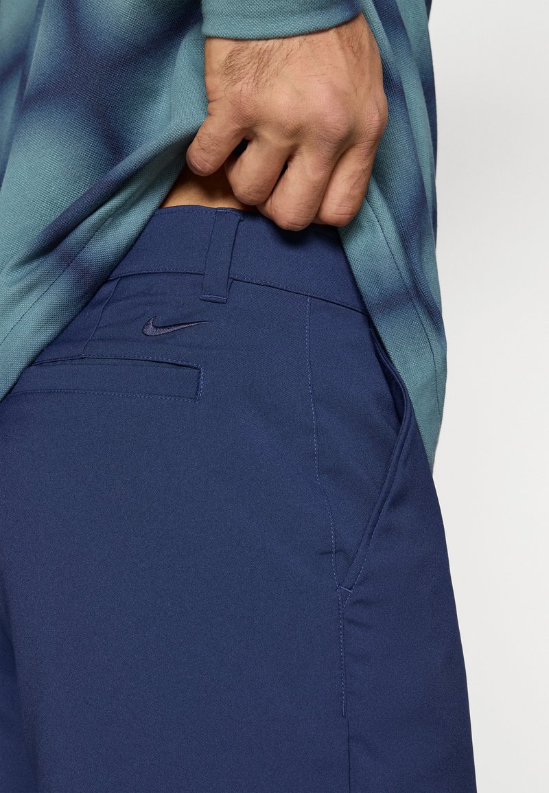 Die Nike navyblauen Sporthosen zeichnen sich durch einen strukturierten Stoff, ein elegantes Design und ein dezentes Logo am Bund aus, das teilweise unter einem Shirt sichtbar ist.