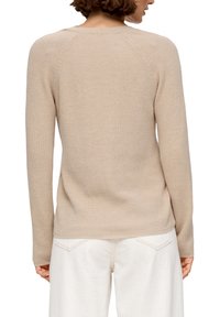 Pull en maille beige avec manches raglan, texture côtelée et col rond. Associé à un pantalon ample de couleur claire.