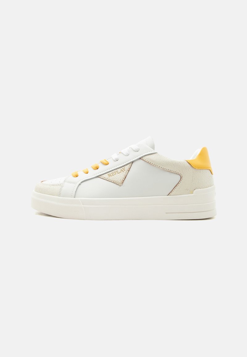 Baskets basses blanches avec détails en daim beige, patch jaune au talon, lacets jaunes et logo "REPLAY" sur le côté.