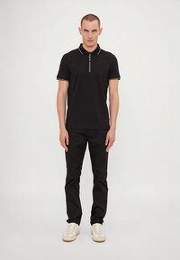 Čierna polokošeľa s bielymi akcentmi a logom. Kombinovaná s čiernymi nohavicami a bielymi teniskami, s priliehavým strihom a klasickým dizajnom.