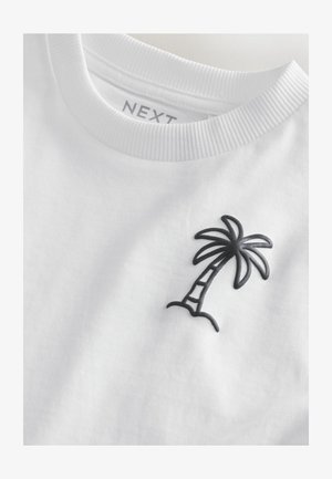 Biele tričko s krátkym rukávom s čiernym vyšívaným obrázkom palmy na ľavej strane hrudníka. Rebrovaný výstrih a mäkká bavlnená tkanina.