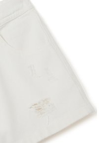 Falda de mezclilla blanca con parches deshilachados, de forma clásica y con un bolsillo frontal. La tela tiene una textura suave y un acabado liso.