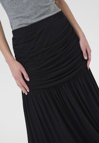 Zwarte maxi-jurk met een gerimpeld, hooggeplaatste ontwerp, gemaakt van zachte, vloeiende stof, met een geraffineerde zoom en een gladde textuur.