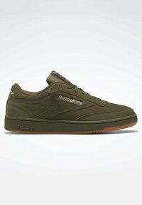 Sneaker Reebok verde oliva a basso profilo con lace-up anteriore, texture in suede e suola in gomma, con logo Reebok e bandiera britannica sul lato.