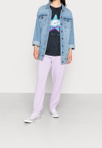 Džínová bunda se světle modrým omylem, černé tričko s grafikou a vzorem hvězd, levandulové tepláky a světle růžové tenisky.