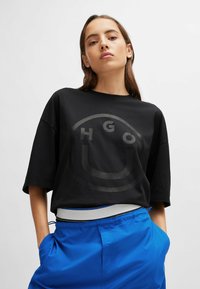 Sort oversized t-shirt med et rundt grafisk motiv i en lysere nuance, korte ærmer og rund halsudskæring, parret med blå shorts.