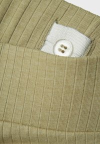 Tissu beige côtelé avec une finition de poche blanche, comportant un bouton transparent et deux boutonnières cousues, mettant en avant la texture et le détail du design.