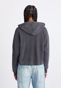 Sweatshirt à capuche raccourci en gris foncé, fabriqué en tissu doux avec une finition texturée. Présente des épaules tombantes et une coupe décontractée.