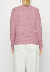 Rosa gestrickter Pullover mit strukturierter Oberfläche, langen Ärmeln und rundem Ausschnitt, kombiniert mit hellfarbenen Jeans mit weitem Bein.