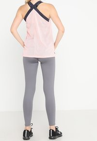 Top in rete rosa con spalline incrociate blu, abbinato a leggings grigi aderenti e scarpe da ginnastica nere. Design semplice e vestibilità comoda.