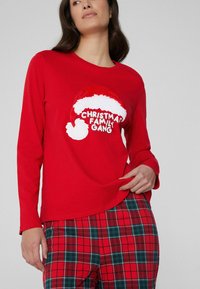 Rode top met lange mouwen met een witte kerstmanmuts en de tekst "Christmas Family Gang". Bijpassende geruite pyjamabroek in rood, groen en wit.