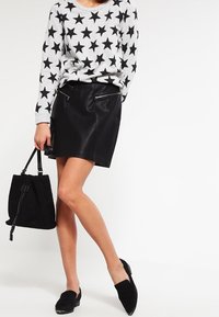 Suéter gris con patrón de estrellas negras, combinado con una minifalda de cuero negra. Un bolso de ante negro y zapatos completan el look.