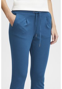 Blå sweatpants gjorda av mjukt tyg, med dragsko i midjan, sidofickor och subtila veck för extra detalj.